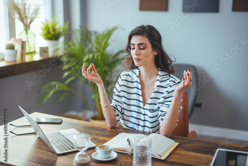 Foto Young woman near the laptop, practicing meditation at the office desk, in front