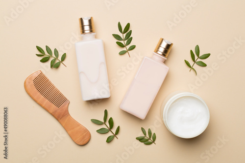 Shampoo and conditioner with herbal extract and comb on color background, top view