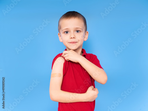 Happy boy child on his shoulder with a patch on his arm after vaccination on a blue background, The concept of vaccination against coronavirus or COVID-19