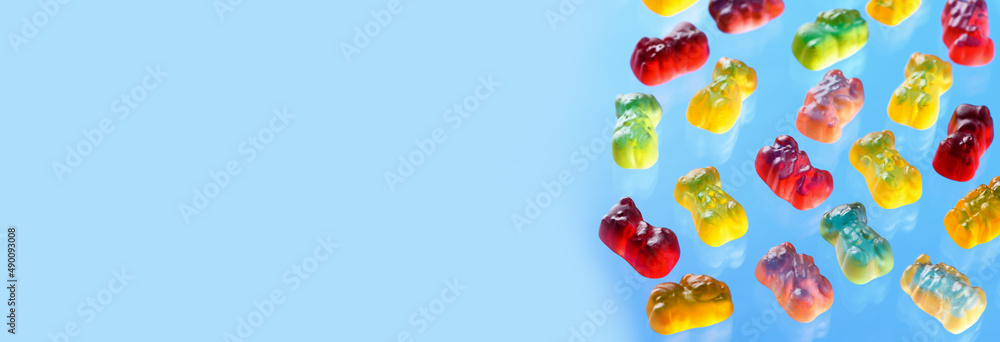 Multicolored flying gummy bears on blue background. Banner