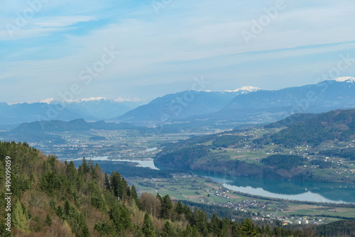 Fototapeta Naklejka Na Ścianę i Meble -  Scenic view on the Drava river in the Rosental valley on the way to Sinacher Gupf in Carinthia, Austria. Forest in early spring. The Hohe Tauern mountain range can be seen in the back. Sunny day. Hike