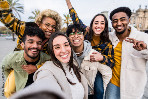 Multiracial group of friends taking selfie picture together with smart mobile phone outside - Happy teens walking on city street enjoying weekend activities - Happy people and youth lifestyle concept photo