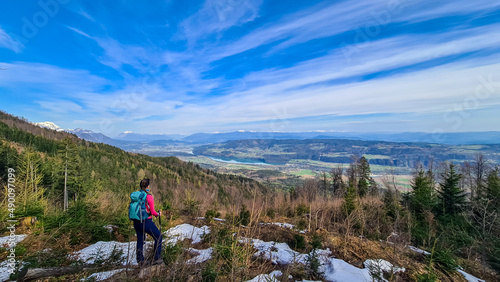 Woman with backpack and a scenic view on the Drava river in the Rosental valley on the way to Sinacher Gupf in Carinthia, Austria. Forest in early spring. Austrian Alps mountain ranges on sunny day