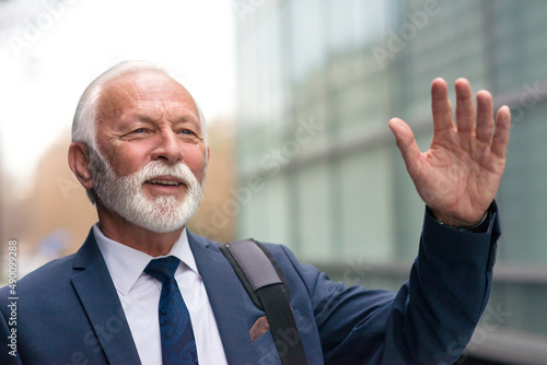 Senior businessman waving to someone on the street in front of the corporate building.