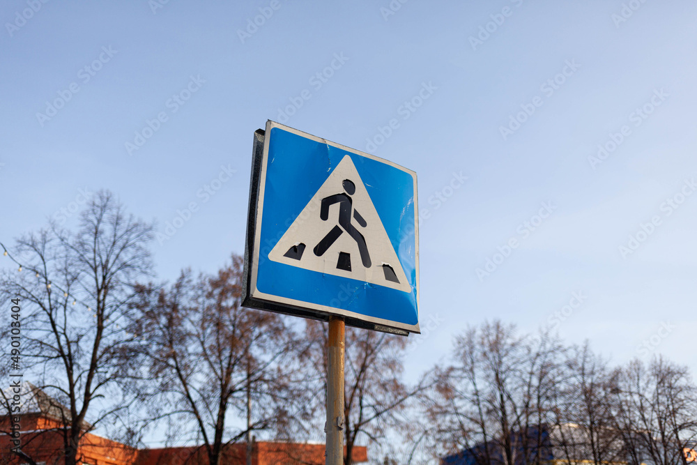 The road sign of a pedestrian crossing in the city at the intersection. A worn sign on warns drivers about a pedestrian crossing. Caution on the road.