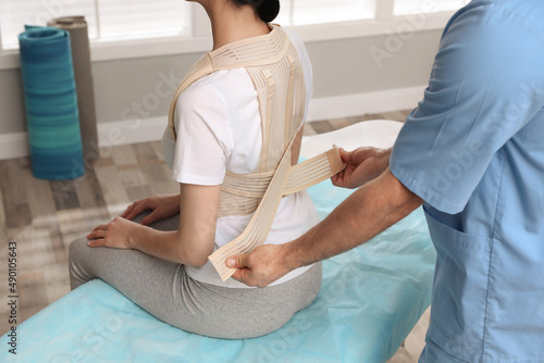 Orthopedist helping patient to put on posture corrector in clinic, closeup. Scoliosis treatment photo