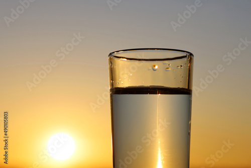 Clean water in drinking glass on sunset sky background. Concept of health and freshness, thirst, water purification