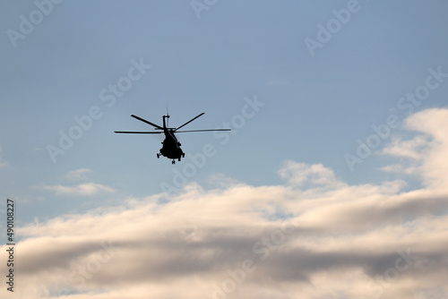 Silhouette of military helicopter in flight in blue sky with clouds