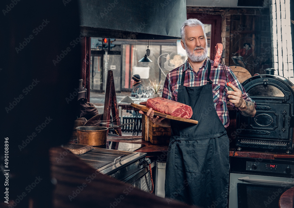 Confident old chef posing in in stylish meat grocery