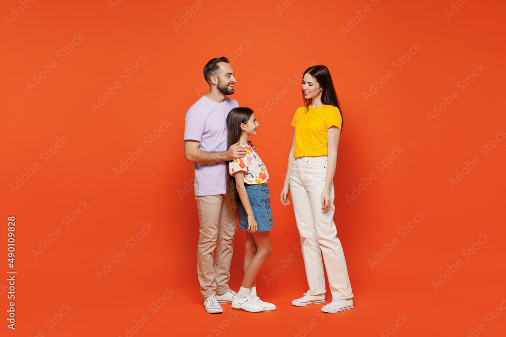 Full body side view young fun smiling happy parents mom dad with child kid daughter teen girl in basic t-shirts cuddling isolated on yellow background studio. Family day parenthood childhood concept Full body side view young fun smiling happy parents mom dad with child kid daughter teen girl in basic t-shirts cuddling isolated on yellow background studio. Family day parenthood childhood concept