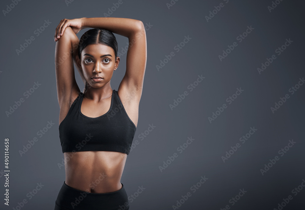 Fototapeta premium Lets start this workout with a few powerful stretches. Studio portrait of a sporty young woman stretching her arms against a grey background.