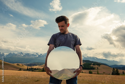 Man standing in in summer Altai mountains in Kurai steppe and holding circle mirror. Creative travel concept photo
