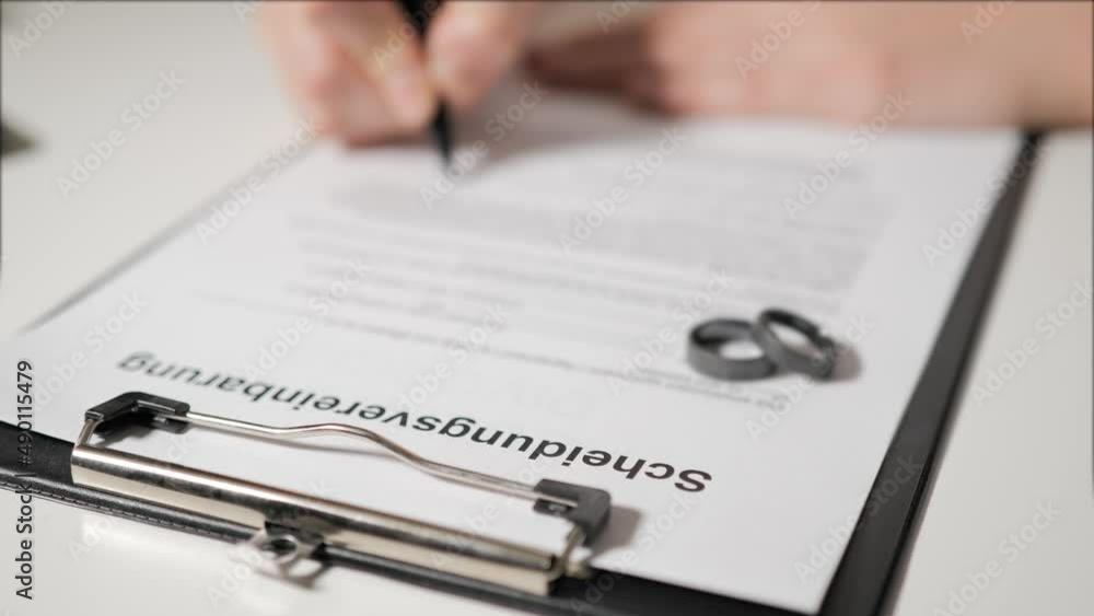 Divorce agreement in German-speaking languages. Hands of husband or wife sign divorce papers. In the foreground are titanium wedding rings. Divorce agreement in German-speaking languages. Hands of husband or wife sign divorce papers. In the foreground are titanium wedding rings.