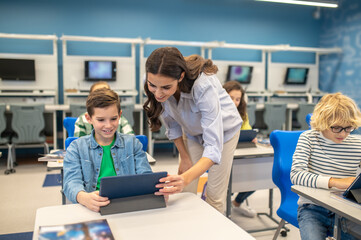 Woman leaning over looking into boys tablet