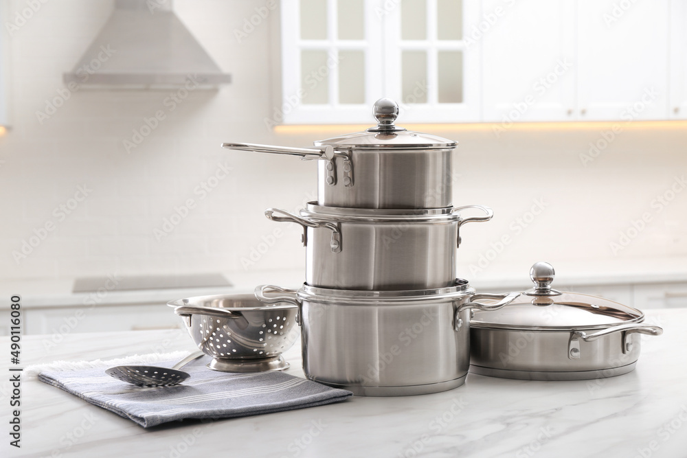 Set of stainless steel cookware and kitchen utensils on white table indoors Set of stainless steel cookware and kitchen utensils on white table indoors