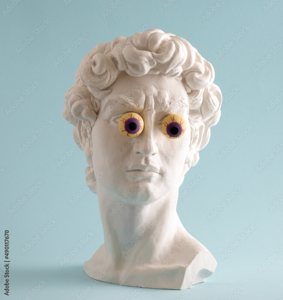 Plaster statue of David's head with bulging eyes on blue background