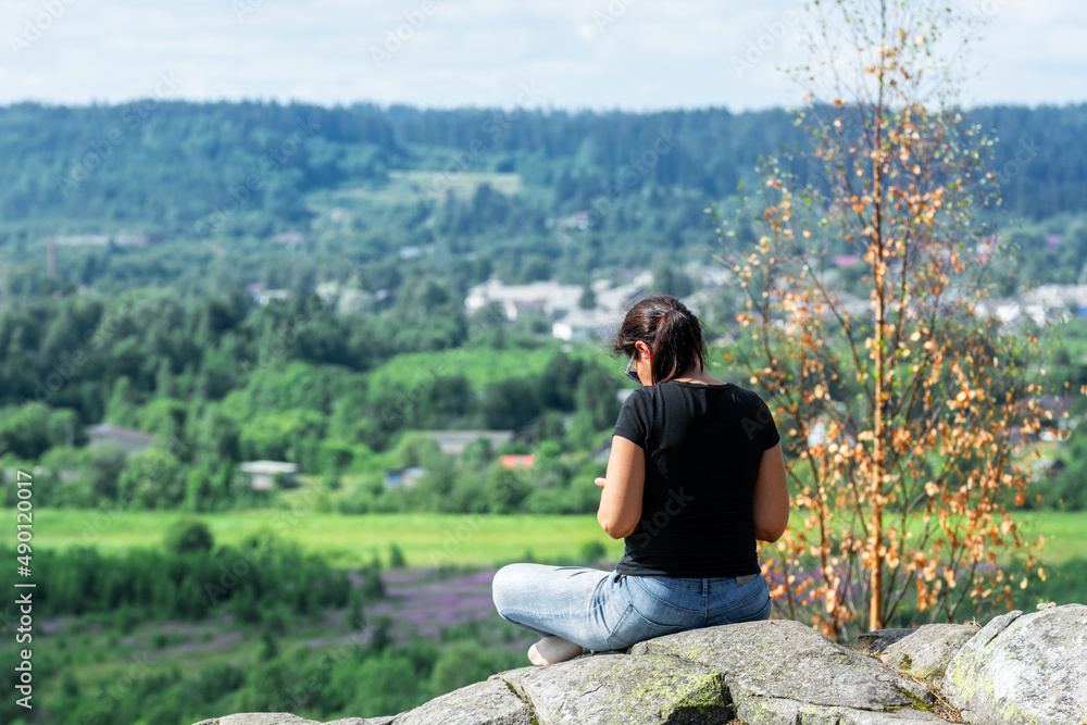 Young woman sits on the rocky surface of Mount Paasonvuori near the town of Sortavala in the Republic of Karelia. Young woman sits on the rocky surface of Mount Paasonvuori near the town of Sortavala in the Republic of Karelia.