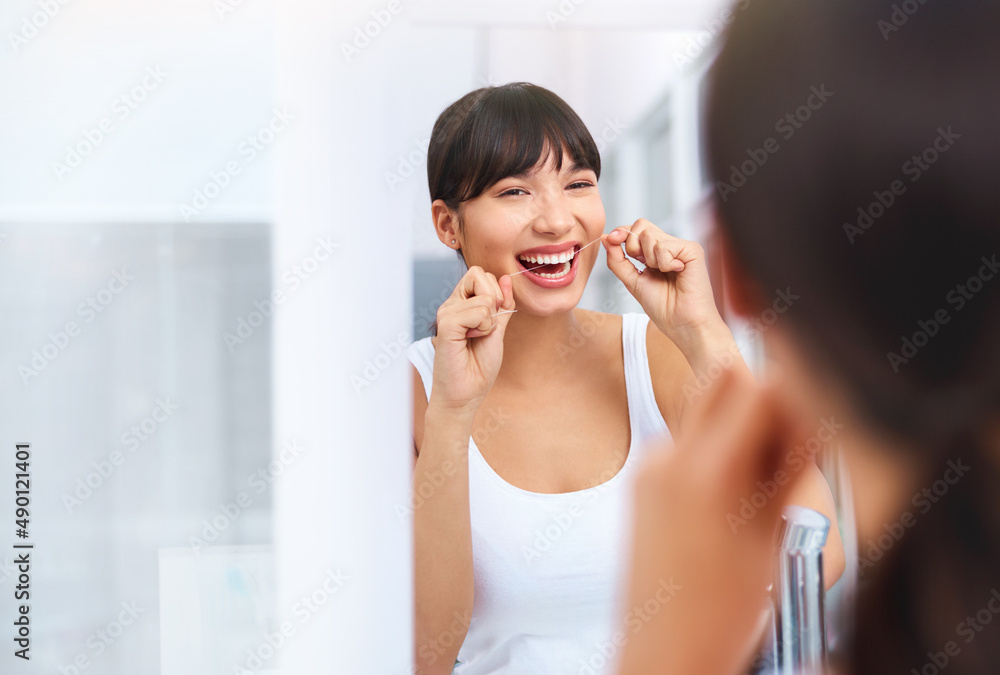 Flossing away. Shot of a cheerful attractive young woman flossing her teeth while looking at her reflexion in a mirror at home. Flossing away. Shot of a cheerful attractive young woman flossing her teeth while looking at her reflexion in a mirror at home.