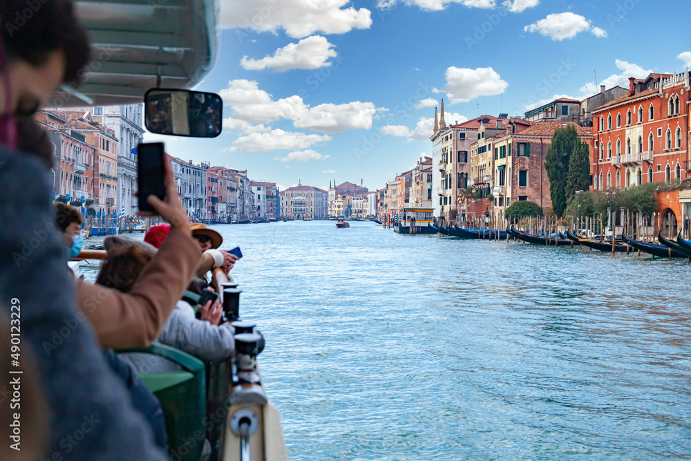 View of the Grand Canal of Venice from a ferry that transports tourists who take pictures with their smartphone