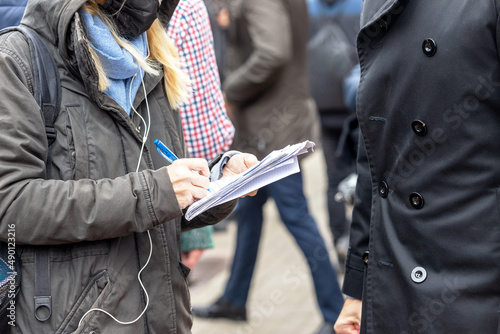 Female journalist wearing protective face mask against coronavirus COVID-19 disease writing notes at news conference or media event