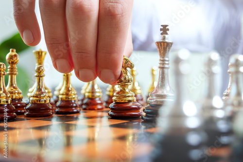 A businessman is holding a chess gold piece of a knight, about to make a move. Game of chess, concept of confrontation, strategic planning, tactic.