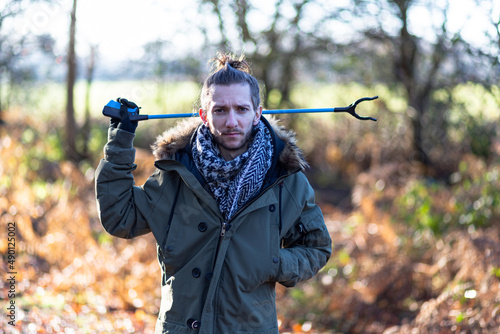 A portrait of a young bearded man with a litter picker ready to do a litter pick and clean up the countryside. Litter pick, rubbish, environmental concept