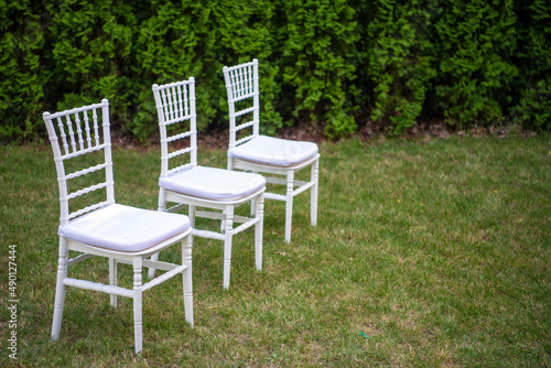 Rows of empty white luxury chairs sitting on a green lawn before a wedding ceremony in summer. © Dragan