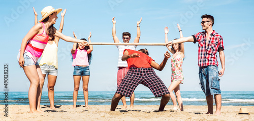 Multicultural friends group having fun together with limbo game at beach vacation - Summer joy life style concept with young multi ethnic people playing on spring break vacation - Bright filter photo