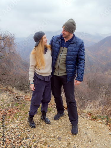 A man and a woman in walking clothes embracing stand against the backdrop of the autumn Caucasian mountains on a foggy day. Traveler couple in love