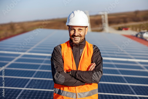 A happy proud worker standing on the roof with solar panels and supporting eco living.