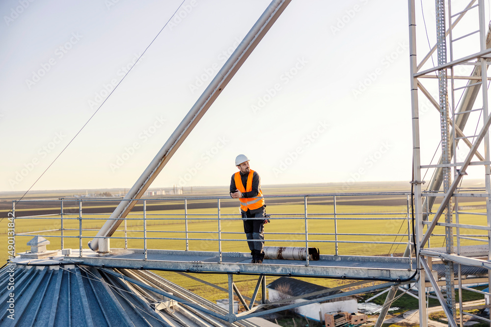An industry worker standing on top of the silo and taking a break.