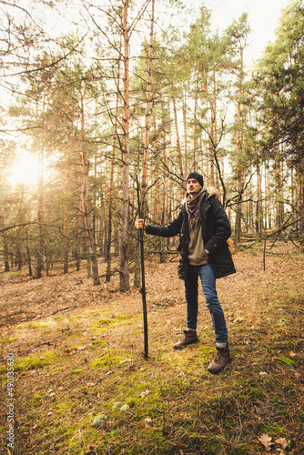 Mystic gamekeeper standing with magic stick on the green moss in the pine forest in the sunlight.