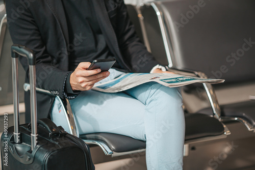 Passenger in an airport lounge waiting for flight aircraft. Young man with smartphone in airport waiting for landing