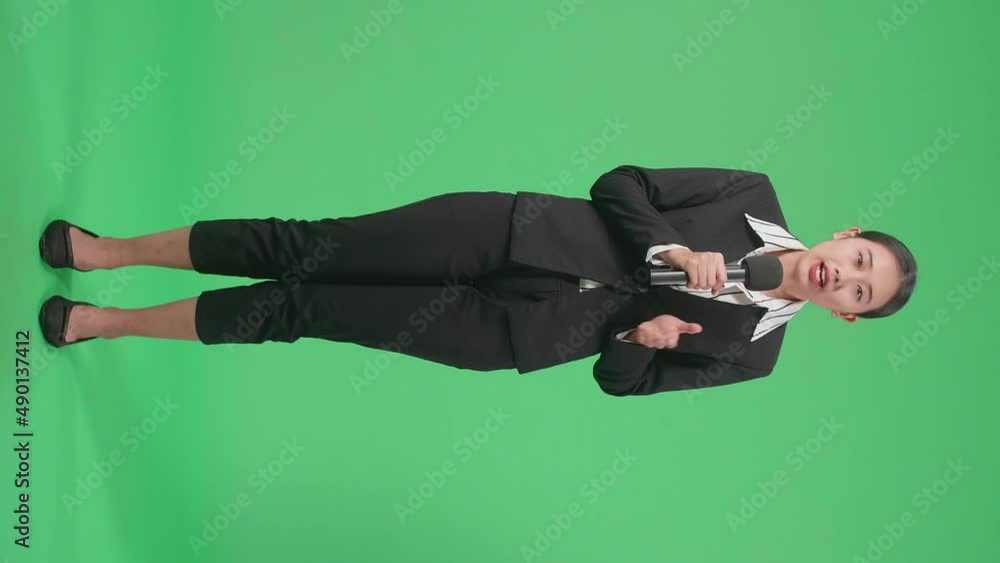 Full Body Of Asian Woman Journalist Pointing On Something While Speaking Into A Microphone On The Green Screen
