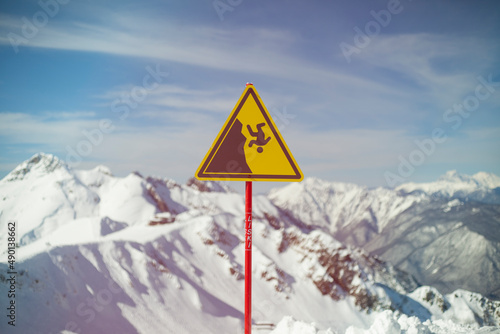 Sign on background of mountains. Sign warning of danger of falling. Triangle on stick. Symbol on yellow background. Carefully abrupt break.