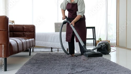 Housewife from cleaning service cleans carpet with vacuum cleaner.