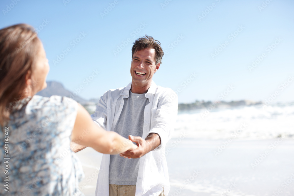 They bring each other so much joy. A happy mature couple holding hands while facing each other on the beach.