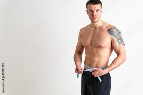 A man measures the waist of a poses against a white background isolated fit muscular background, healthy female bodybuilding woman weight, healthy Oss nutrition athlete, adult sport attractive tape