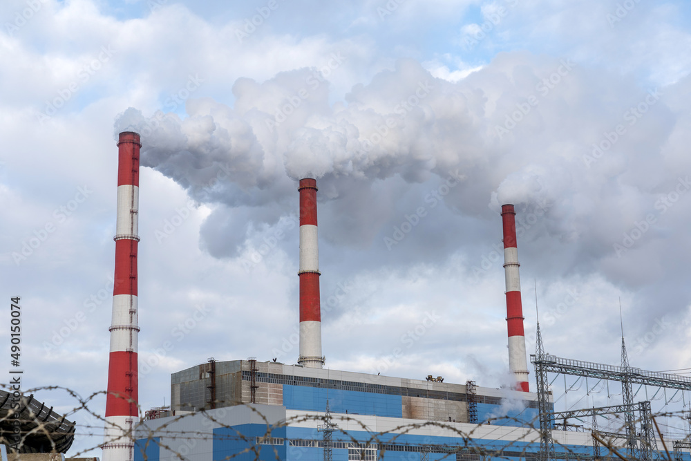 Three factory chimneys emit puffs of smoke polluting the air and the environment.