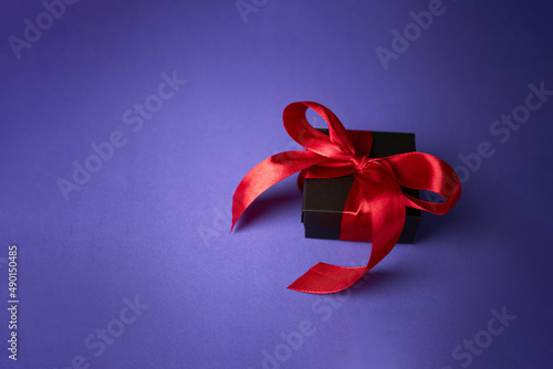 black gift with red ribbon on purple background. Valentine's day. Birthday or Holidays concept. Copy space