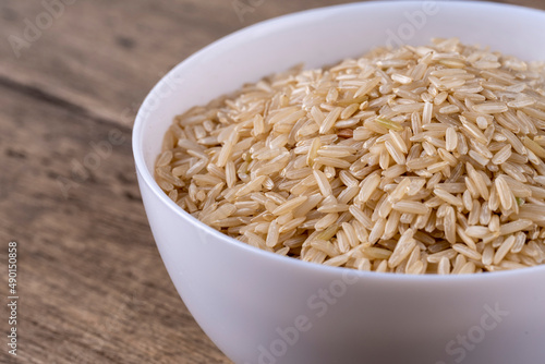 Brown raw Rice Groats In White Bowl Isolated On wooden Background