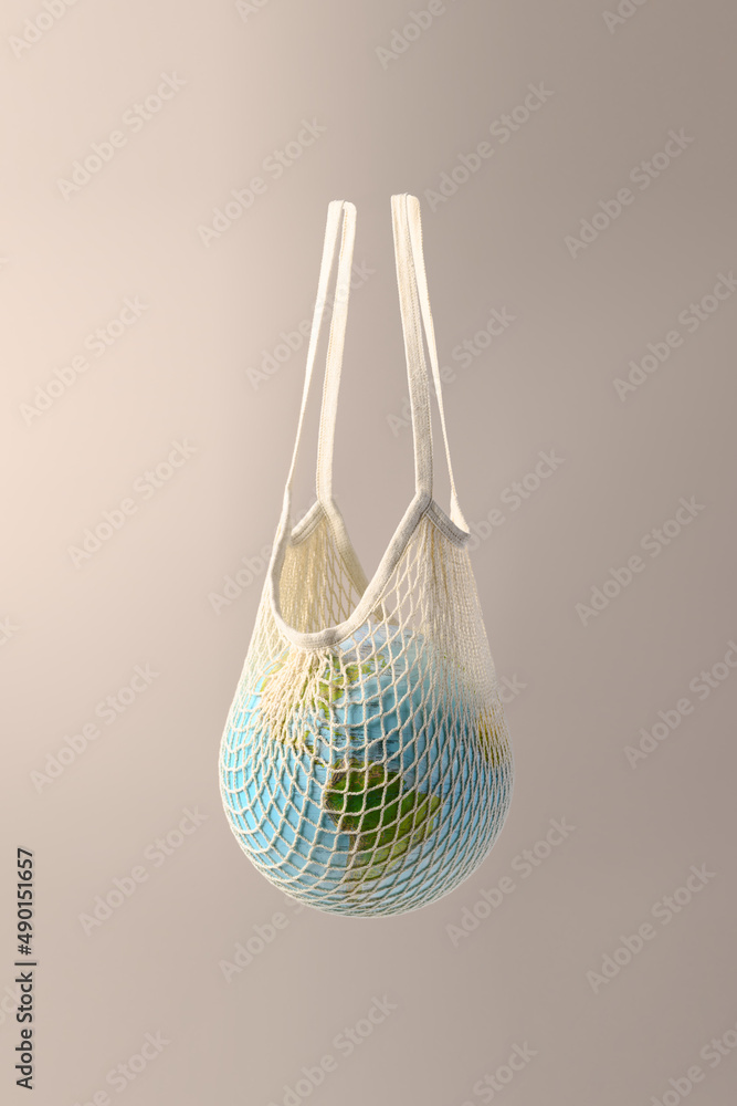 World globe in crochet bag floating in air on beige background. Eco friendly life in the style of zero waste. Earth day save the planet. Stock Photo Adobe Stock