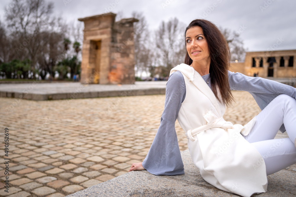 Young brunette girl with beige clothes in the Temple of Debod, Madrid, on a cloudy day