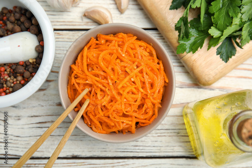 Delicious Korean carrot salad, oil, spices and parsley on white wooden table, flat lay photo