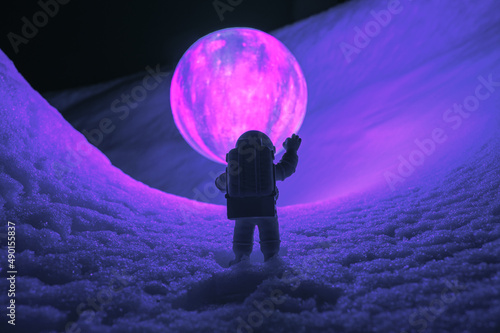 Silhouette of the toy of astronaut against levitating glowing sphere over surface icy planet covered with snow. Concept of space travel, exploration, and colonization