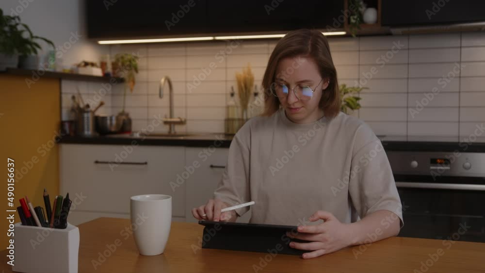 A talented girl concept artist draws on a tablet with a digital display a project of a future casual 3D game, sitting at a table at home in the living room A talented girl concept artist draws on a tablet with a digital display a project of a future casual 3D game, sitting at a table at home in the living room