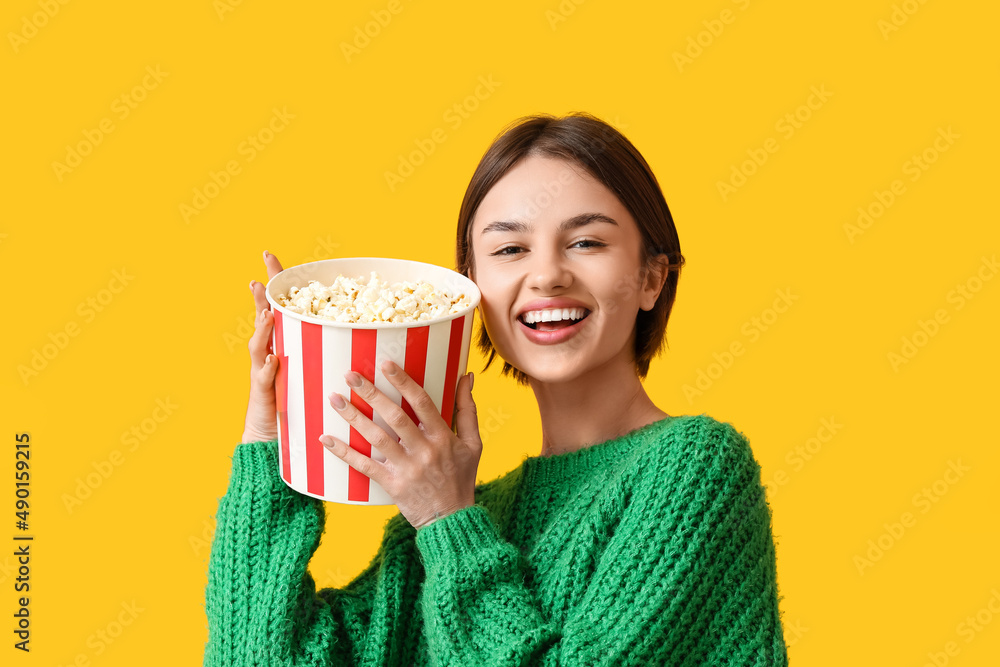 Beautiful young woman with bucket of popcorn on color background