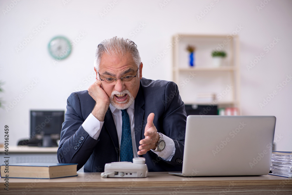 Old male employee speaking on the phone at workplace Old male employee speaking on the phone at workplace