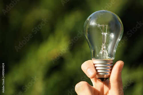 Woman holding incandescent light bulb on blurred green background, closeup. Space for text