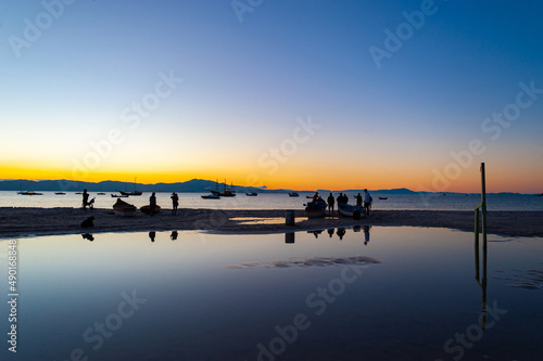 Silhueta entre o mar e a lagoa no por do sol com pessoas ao fundo sem reconhecimento espelhando as imagens na lagoa. photo